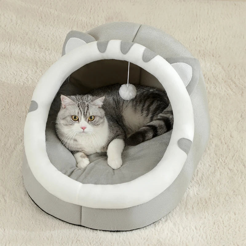 Cat lying in a gray and white pet bed with cat ears on a beige carpet.