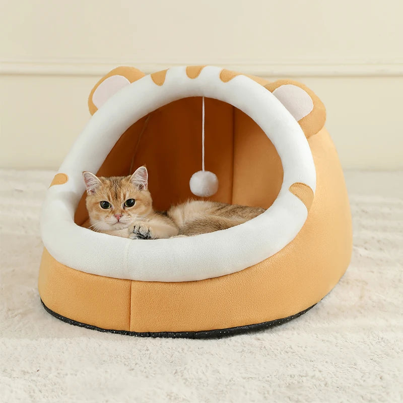 Cat lying in a yellow and white pet bed with a hanging ball toy on a light background


